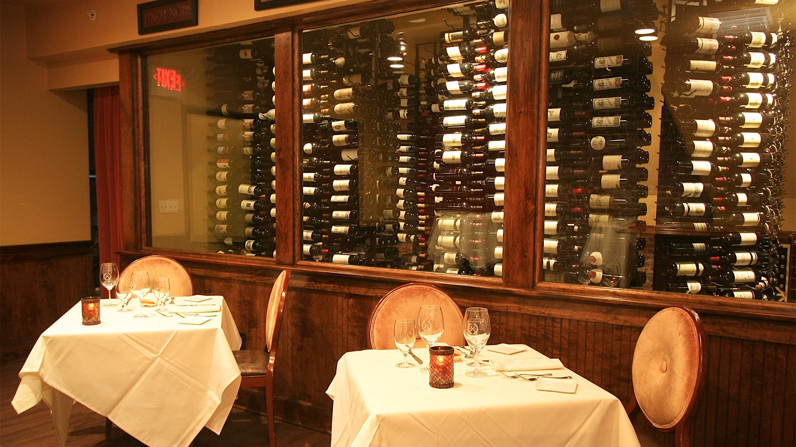 The dining room at Knife and Fork Inn, with tables with white tablecloths and a glass-covered wall of wine bottles